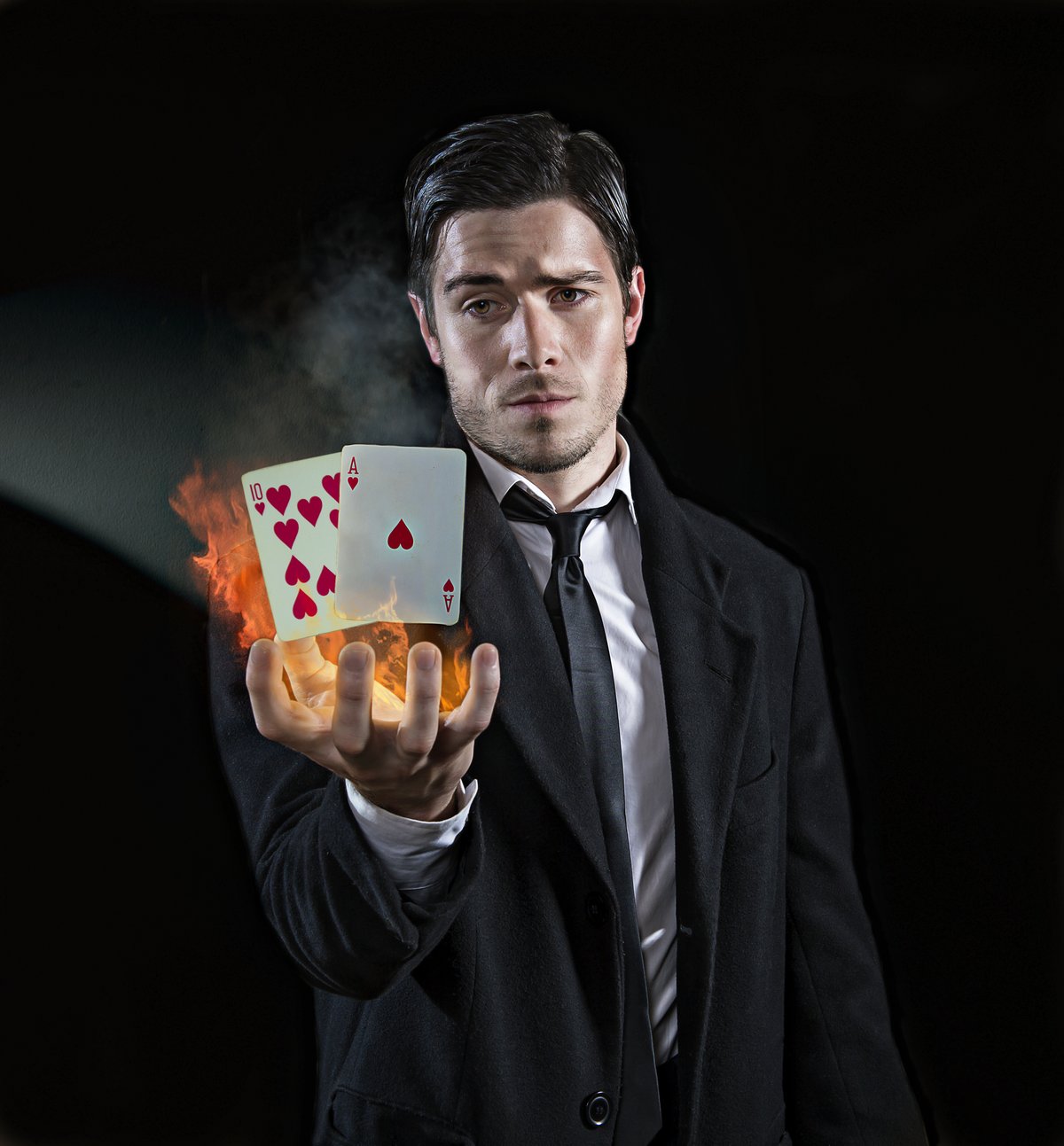 A magician holds a hand of burning playing cards.