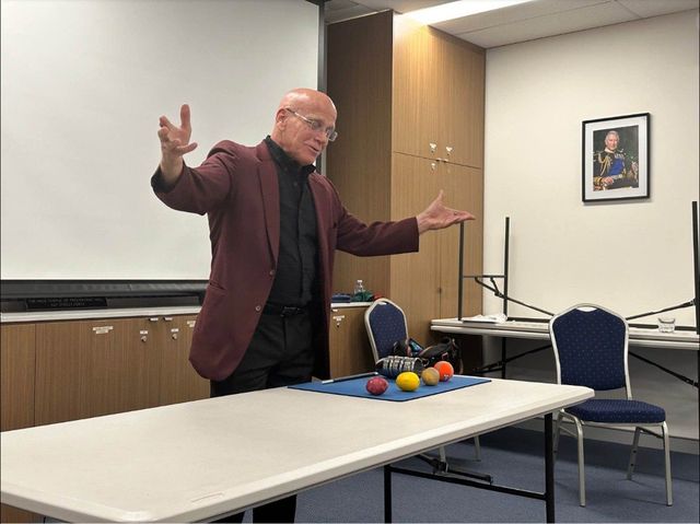 Michael Ammar lecturing, with his signature props on the table