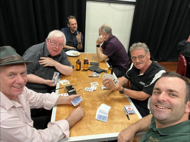 Members sharing card magic around a table at the May 2024 meeting